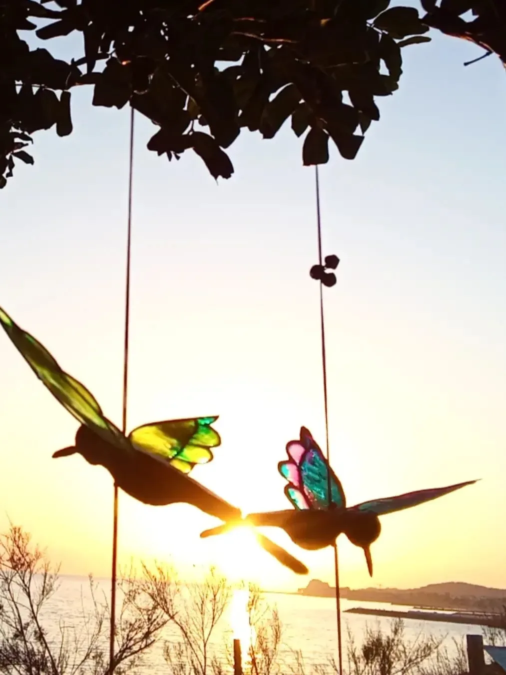Two bird sculptures hanging against sea sunset